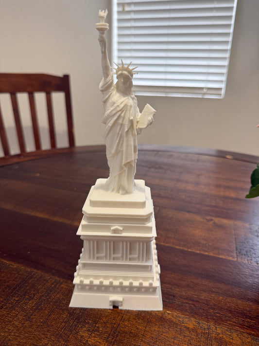 3D printed white Statue of Liberty model on a wooden table, front view showing torch and tablet details