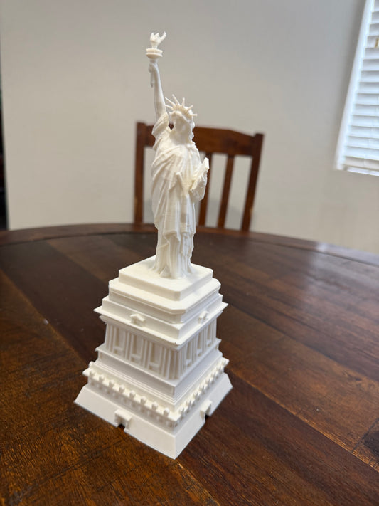 Side angle of a 3D printed Statue of Liberty model in white PLA, highlighting pedestal layers and statue posture.